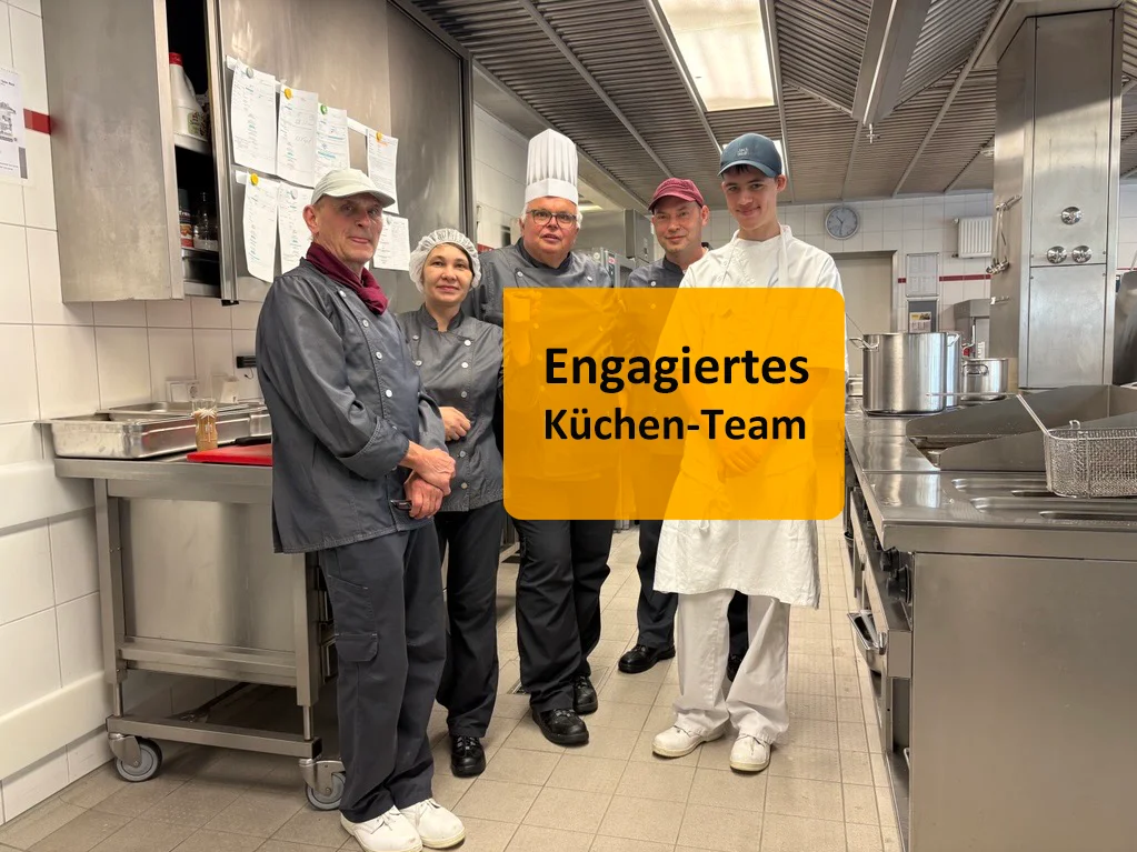 Küchenteam posiert in Uniformen in einer professionellen Großküche, mit Beschriftung.