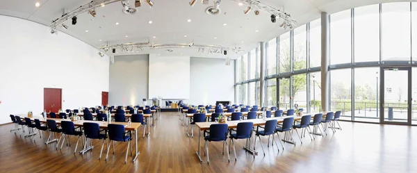 Heller Konferenzraum mit Leinwand, Fensterfront und Stühlen an Tischen.