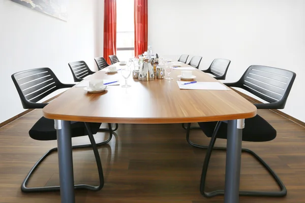 Konferenztisch mit Stühlen, Gläsern, Kaffeetassen und Schreibmaterial.