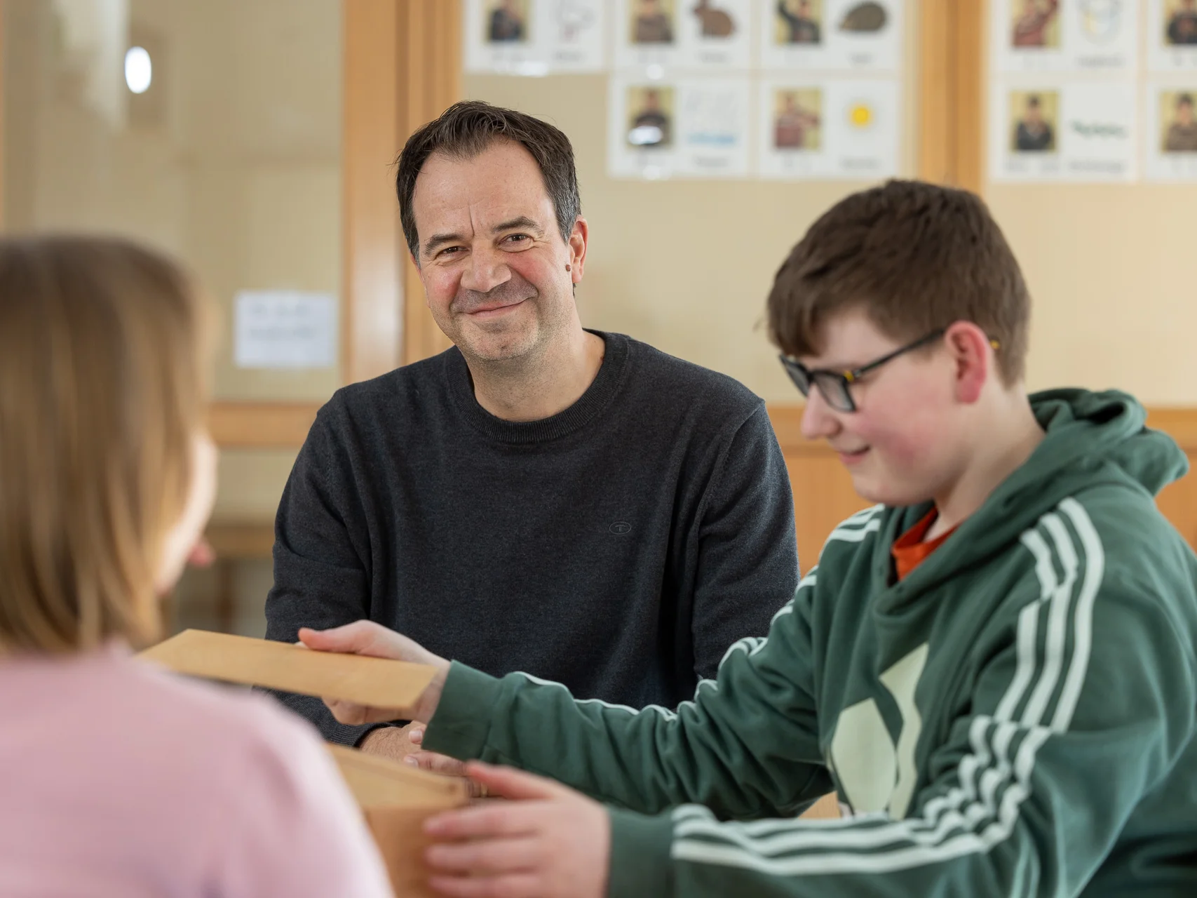 Mann lächelt, während er zwei Kindern beim Spielen mit Holzklötzen zusieht.