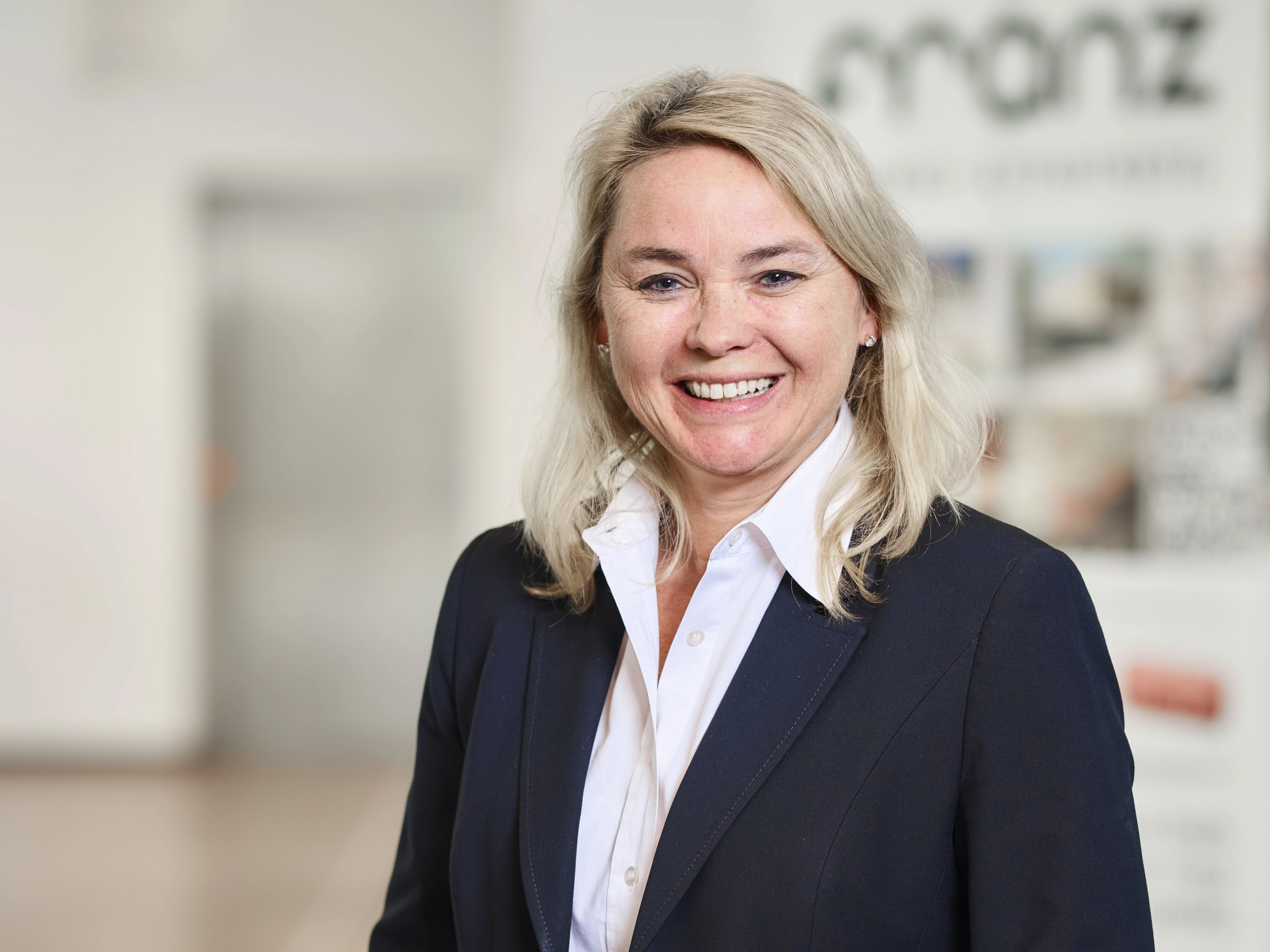 Lächelnde Frau im Business-Outfit vor verschwommenem Hintergrund.