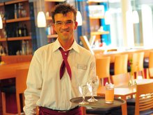 Mitarbeiter des Inklusionsbetriebs Hotel Franz serviert ein Getränk auf einem Tablett