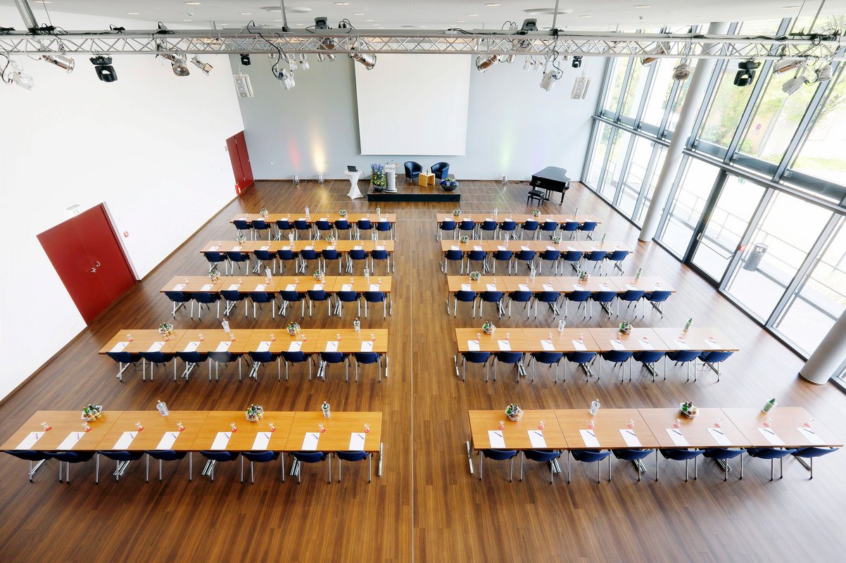 Blick in den Saal, in dem Tisch- und Stuhlreihen stehen.