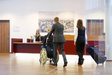 Rollstuhlfahrerin wird von einer Begleitperson an den abgesenkten Rezeptionstresen gefahren