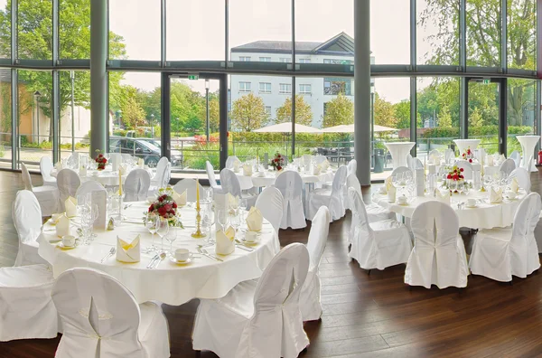 Elegante Hochzeitstische mit weißen Hussen, Blumenarrangements und Panoramafenstern.