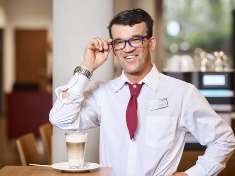 Service-Mitarbeiter mit Behinderung serviert eine Latte Macchiato.