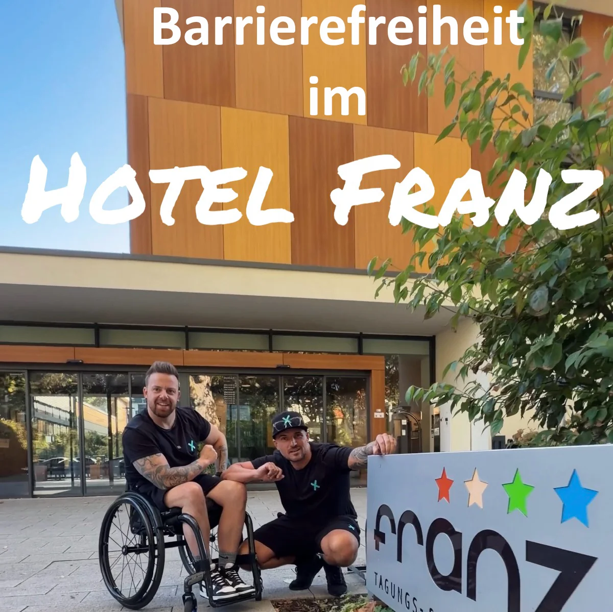 Zwei Personen vor dem Hotel Franz; einer im Rollstuhl, mit Schild und Text "Barrierefreiheit".